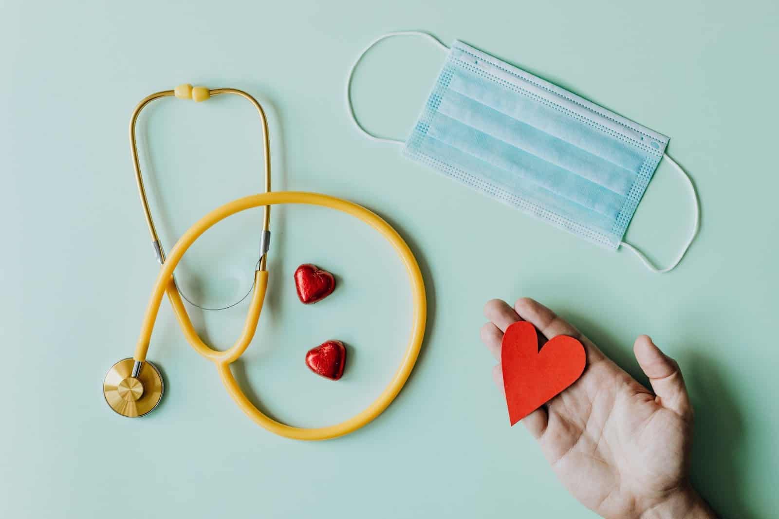 A hand holding a stethoscope on a green background.